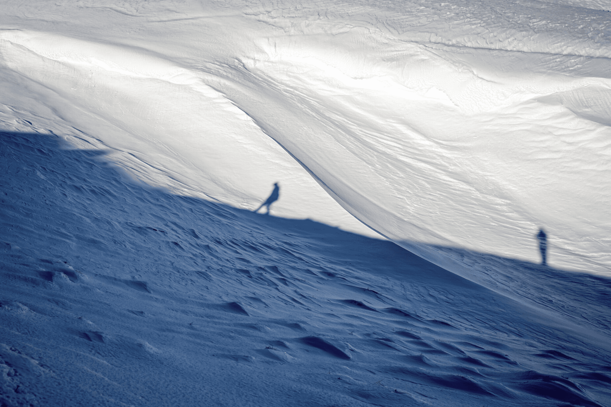 Shadows of people walking along a snow covered slope