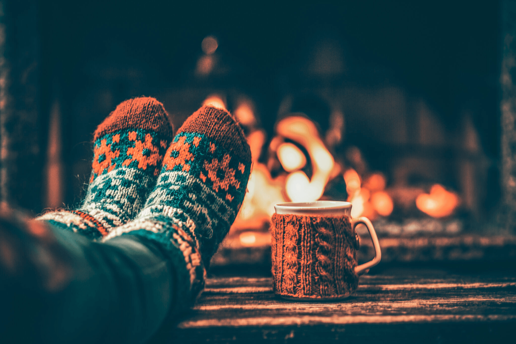 Cozy socks and hot drink by fireplace creating warm winter mood