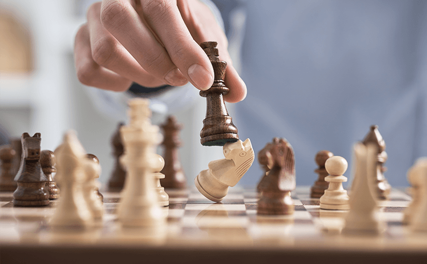 Hand moving a chess piece to capture an opponent’s piece on a chessboard.