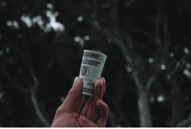 Hand holding a rolled U.S. dollar bill outdoors