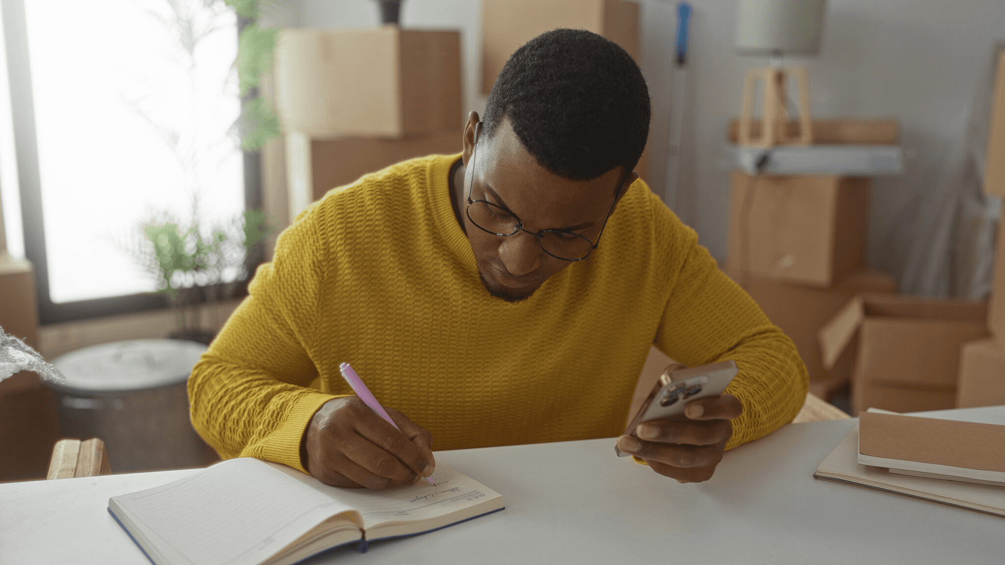 Man writing in notebook while checking phone