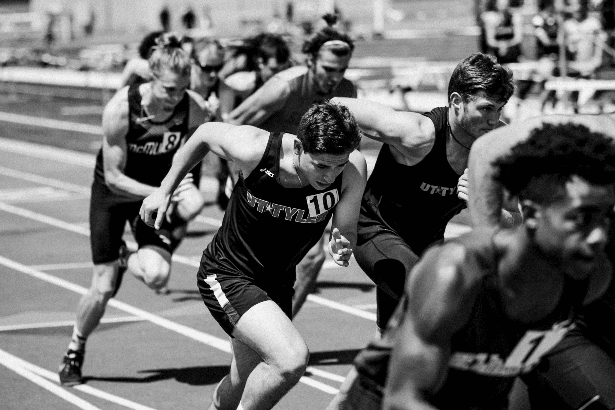 Black-and-white photo of runners launching forward at the start of a track race.