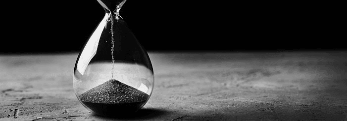 A black-and-white photo of sand falling through an hourglass on a textured surface.