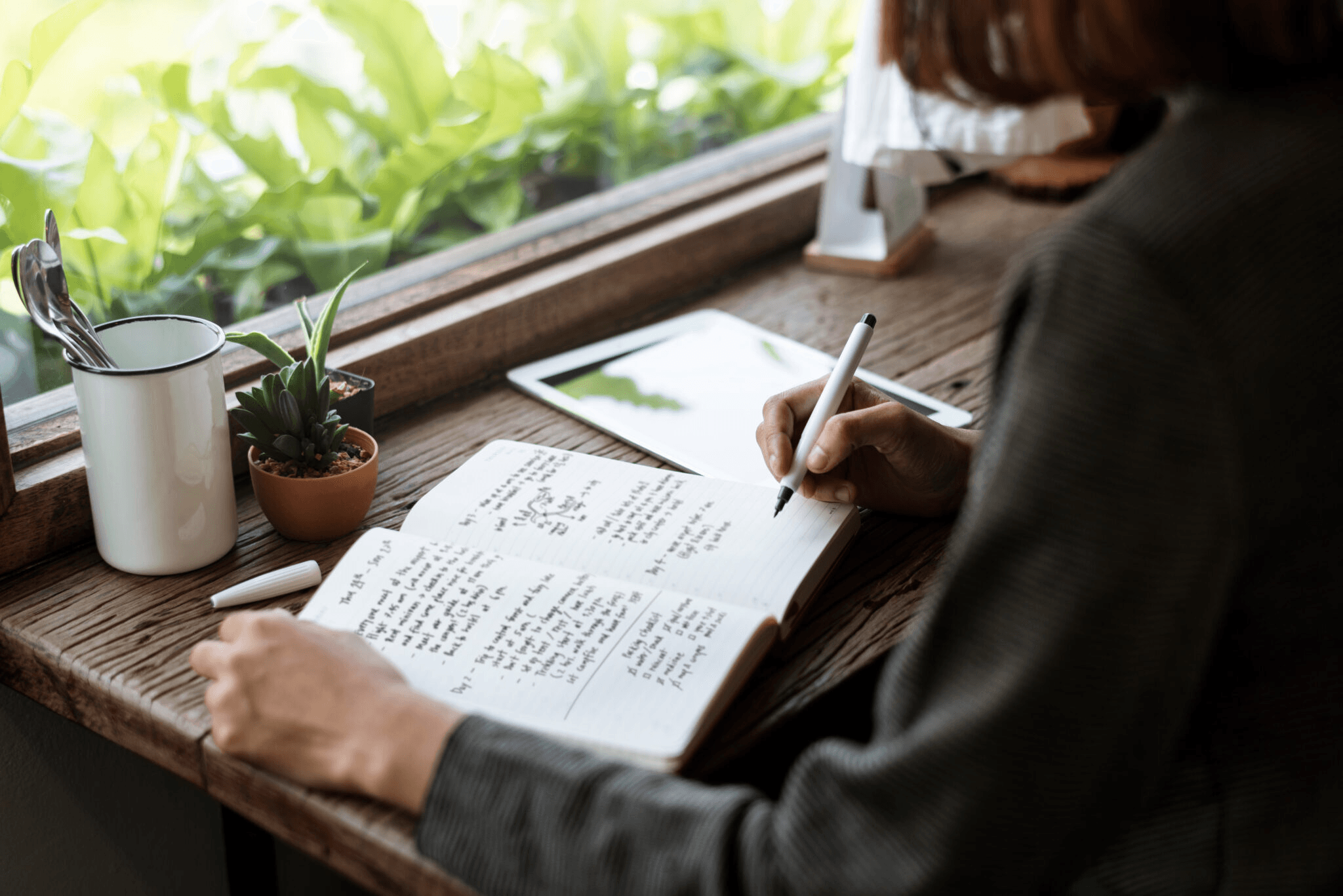 Woman sitting at a desk in front of her window writing into a journal